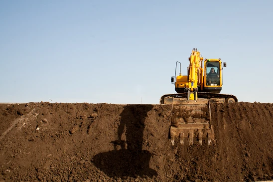 Chantier de terrassement en ext&eacute;rieur avec pelleteuse hydraulique jaune positionn&eacute;e au bord d'une excavation