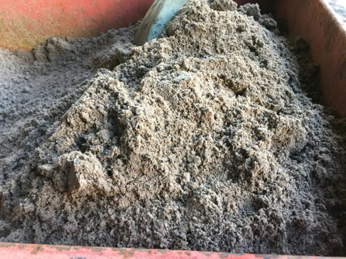 Chantier de construction ext&eacute;rieur avec tas de sable gris-beige fin dans une brouette ou benne rouge